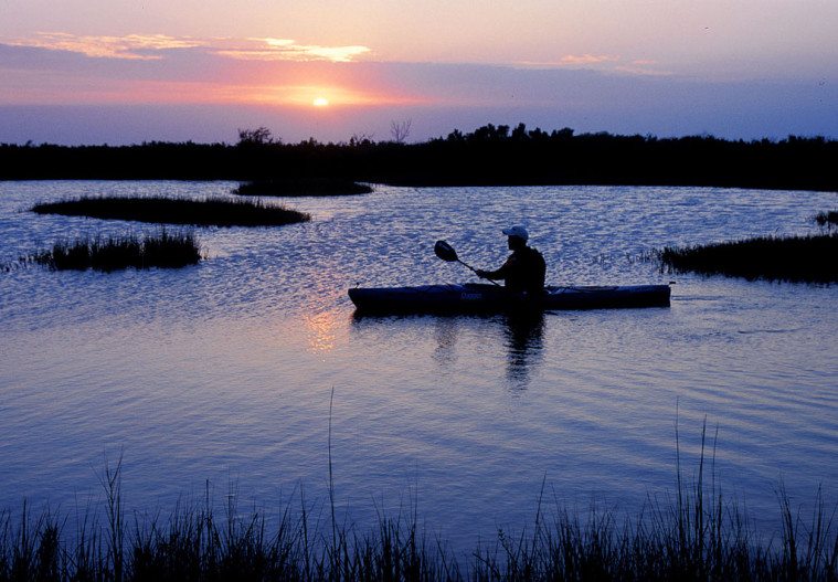A man kayaks in the wetlands of Matagorda Bay Nature Park at sunset.