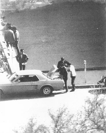 surveillance photo of 3 men opening a trunk of a ford mustang