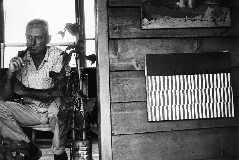 Forrest Bess with his painting Untitled (11A), in his home/studio, Chinquapin Bayou, near East Matagorda Bay, Texas, 1958. The Menil Archives, The Menil Collection, Houston.