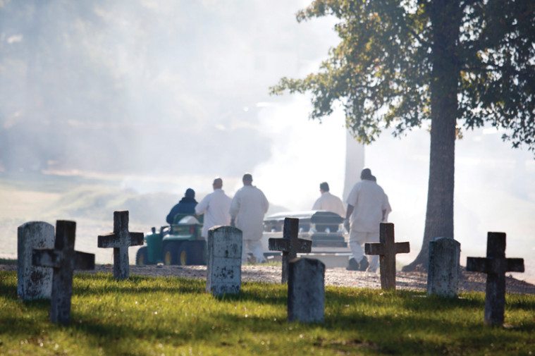 As groundskeepers burn leaves in the distance, inmate pallbearers accompany a coffin down a hill for burial at Captain Joe Byrd Cemetery in Huntsville.