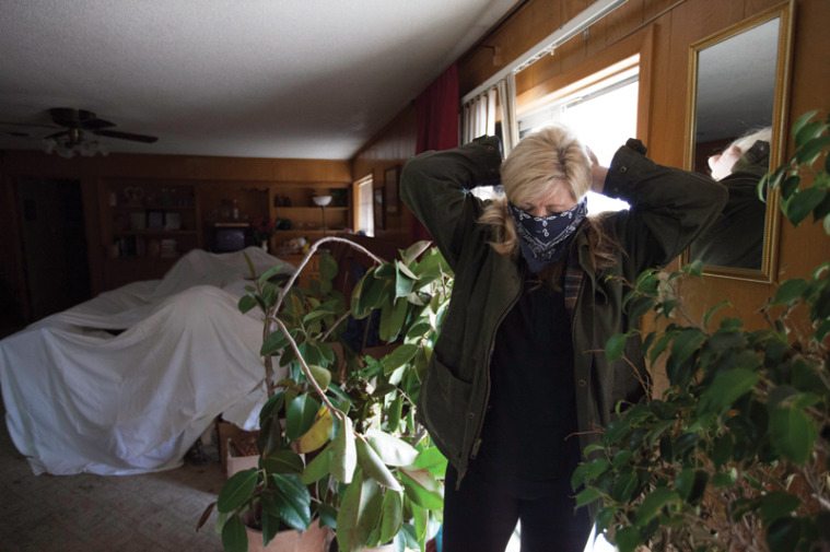 Covering her mouth and nose to keep from inhaling mold, Lori Collins enters her home to retrieve her son’s athletic shoes for school.