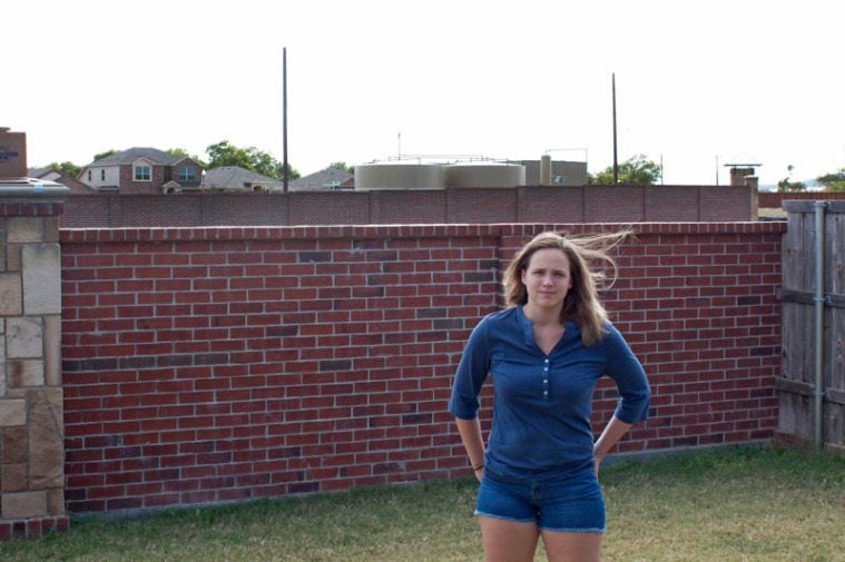 Alyse Ogletree stands in her backyard, the water tanks used for fracking behind her.