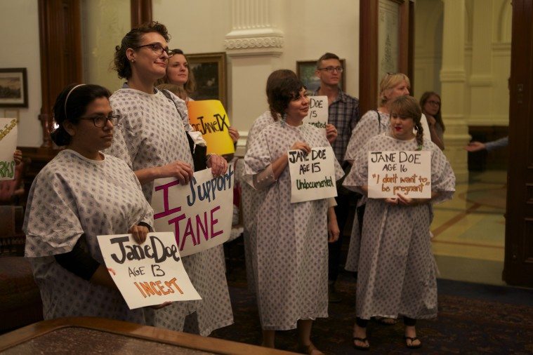 Reproductive rights supporters wear hospital gowns and carry signs reading "I support Jane."
