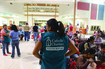 At the McAllen bus station in the summer of 2014, a Catholic Charities volunteer watches while Latin American immigrants prepare to leave for other parts of the country.