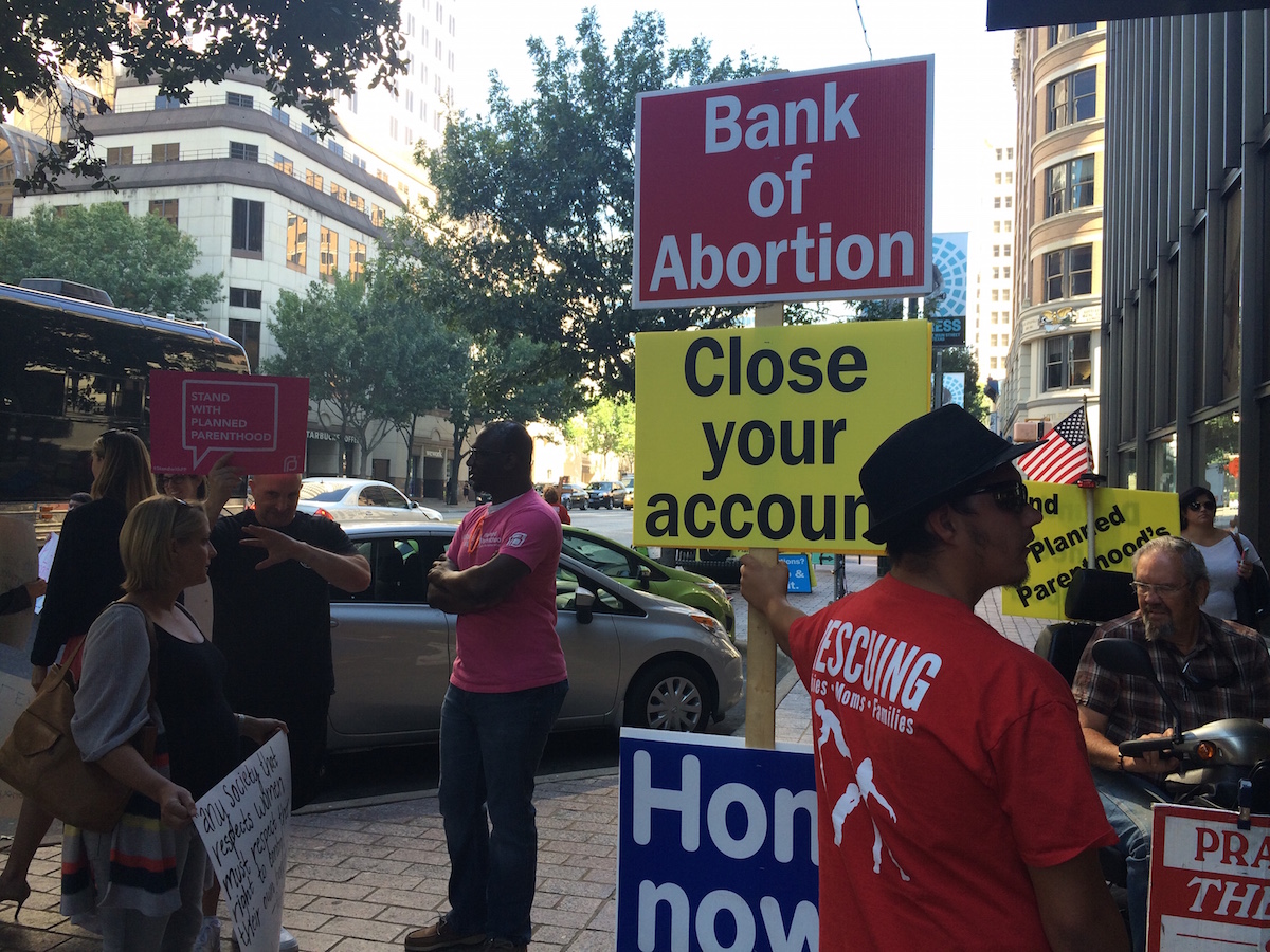 Planned Parenthood supporters and anti-abortion protesters hold signs outside the Bank of America building in downtown Austin.