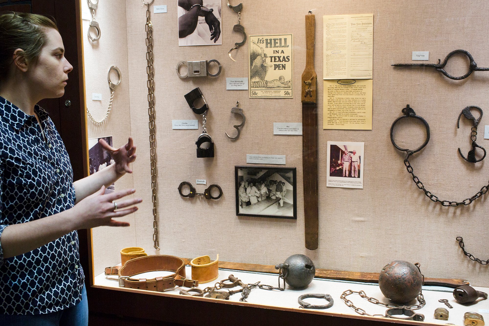 Elizabeth Neucere, assistant curator of collections, with the display on punishment, which includes handcuffs, a ball and chain and the bat, a leather strap with a wooden handle once used to whip inmates. 