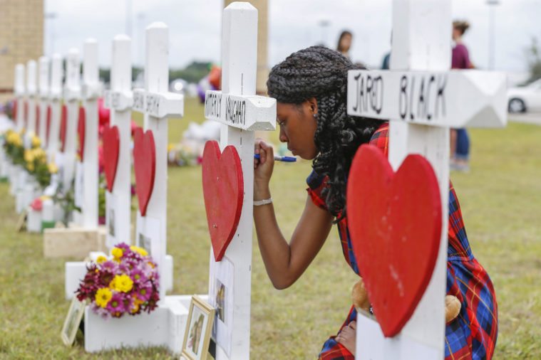 Santa Fe High School freshman Jai Gillard writes messages on each of the 10 crosses in front the school. Gillard witnessed the shooting.