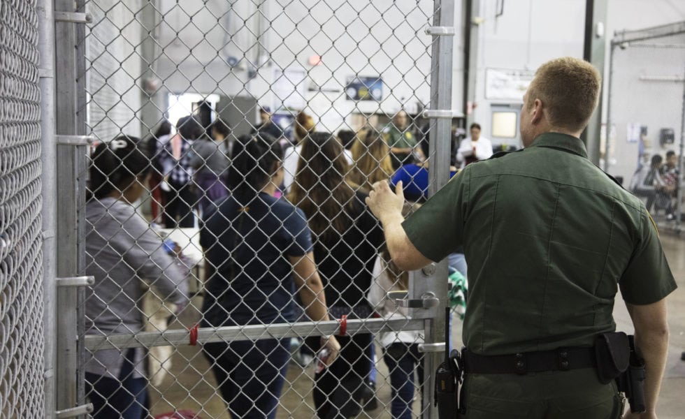 A Border Patrol agent watches as people who've been taken into custody stand in line at a facility in McAllen.