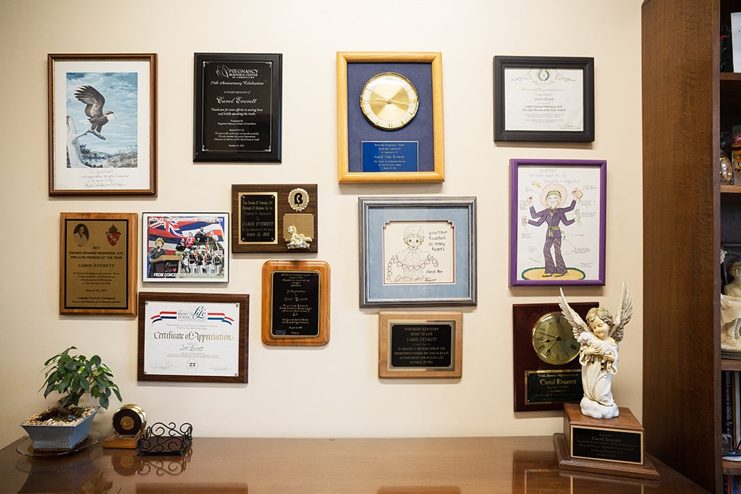 Certificates and plaques from pregnancy centers and anti-abortion groups cover a wall in Carol Everett’s office at the Heidi Clinic.
