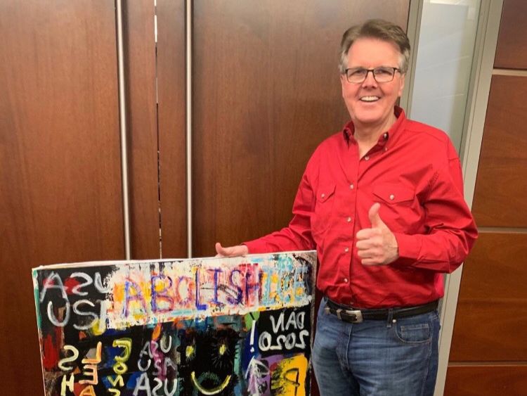 Lieutenant Governor Dan Patrick holds a sign saying "Abolish ICE." High school student Caleb Brock tricked him into holding the sign.