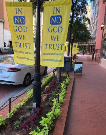 Yellow banners in Fort Worth read "In No God We Trust."
