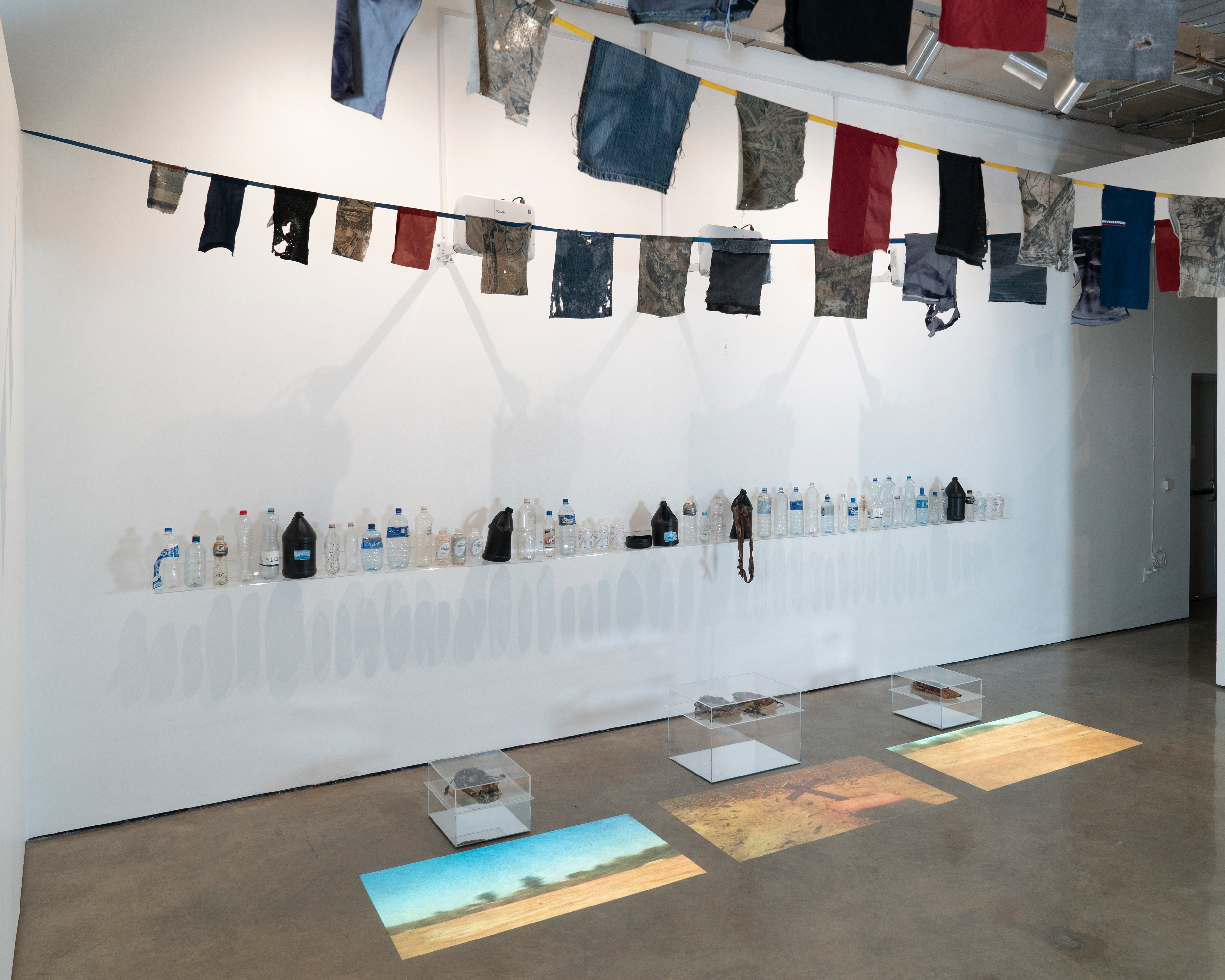 Anne Wallace, Untitled, 2019, Documentary videos; water bottles, clothing and carpet shoes found along migrant trails in the Sonoran desert, Dimensions variable