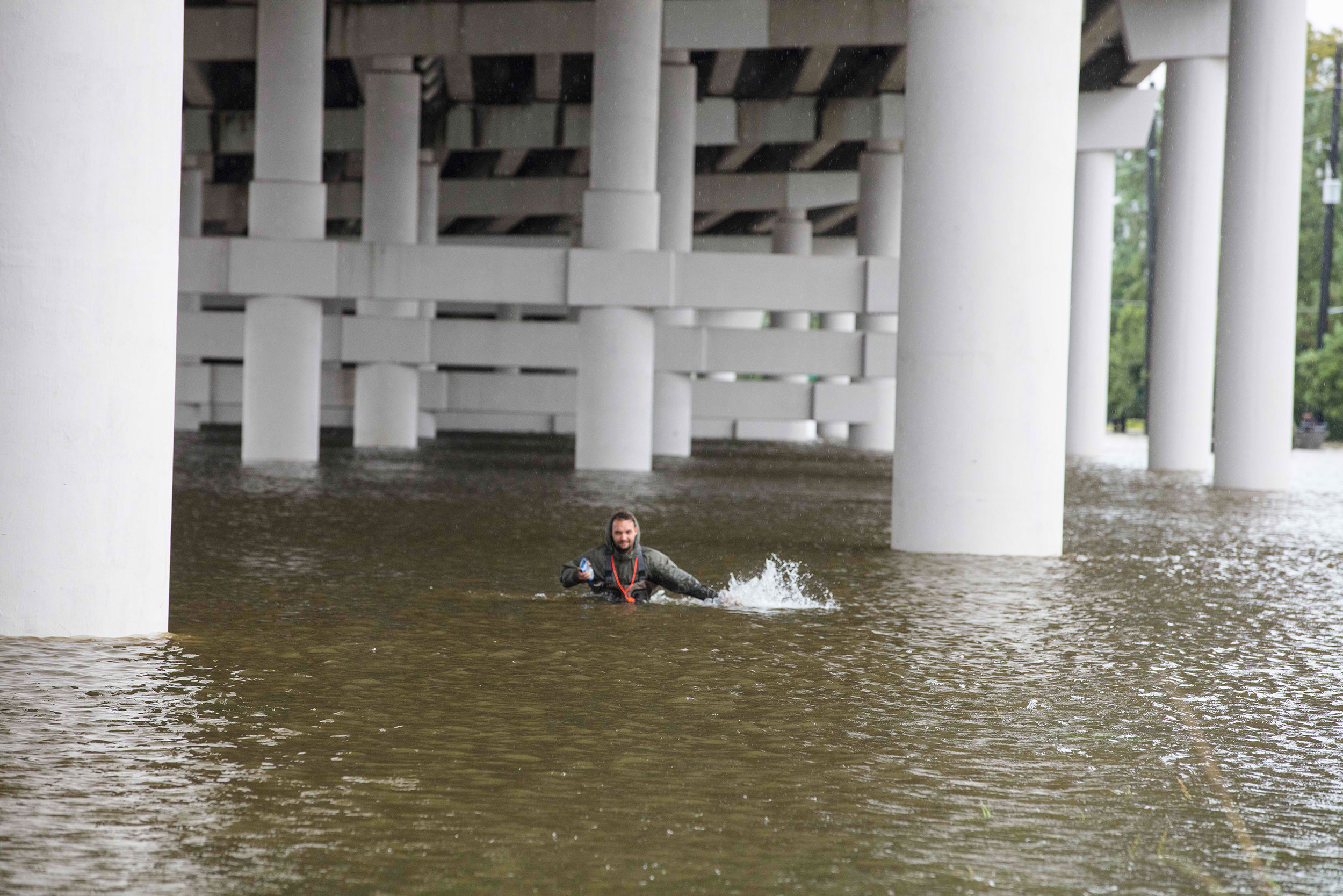 A man wading through chest-high water under an overpass.