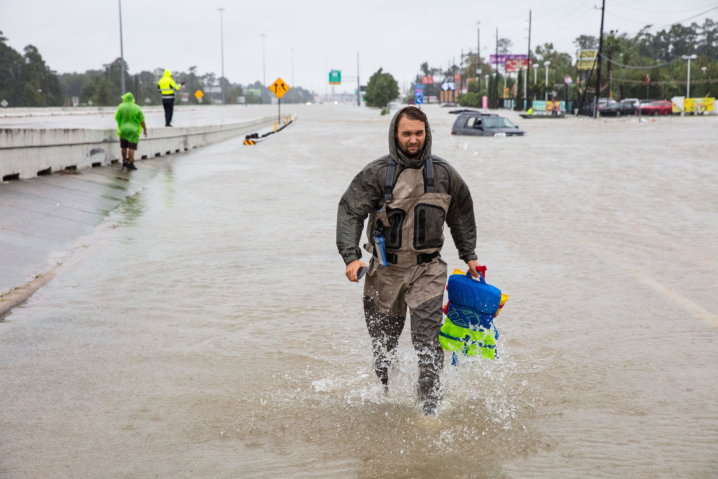 Three rescuers on a street with a flooded car.