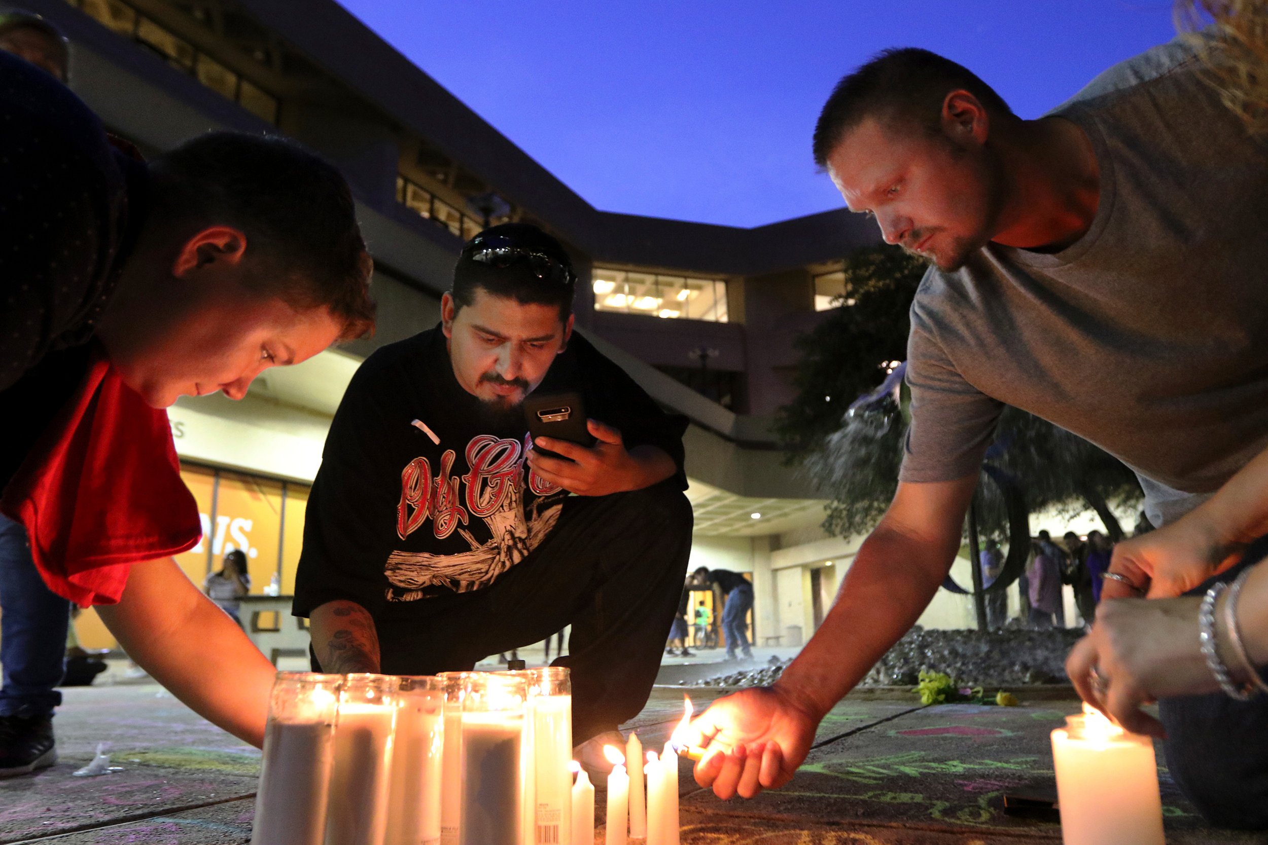 In this Sunday, Sept. 1, 2019, photo Crystal Harris, George Guerrero, and Curtis Patterson light candles in the shape of a cross on the ground of UTPB's quad in Odessa, Texas, to remember those who were killed in a shooting Saturday. (Ben Powell/Odessa American via AP)