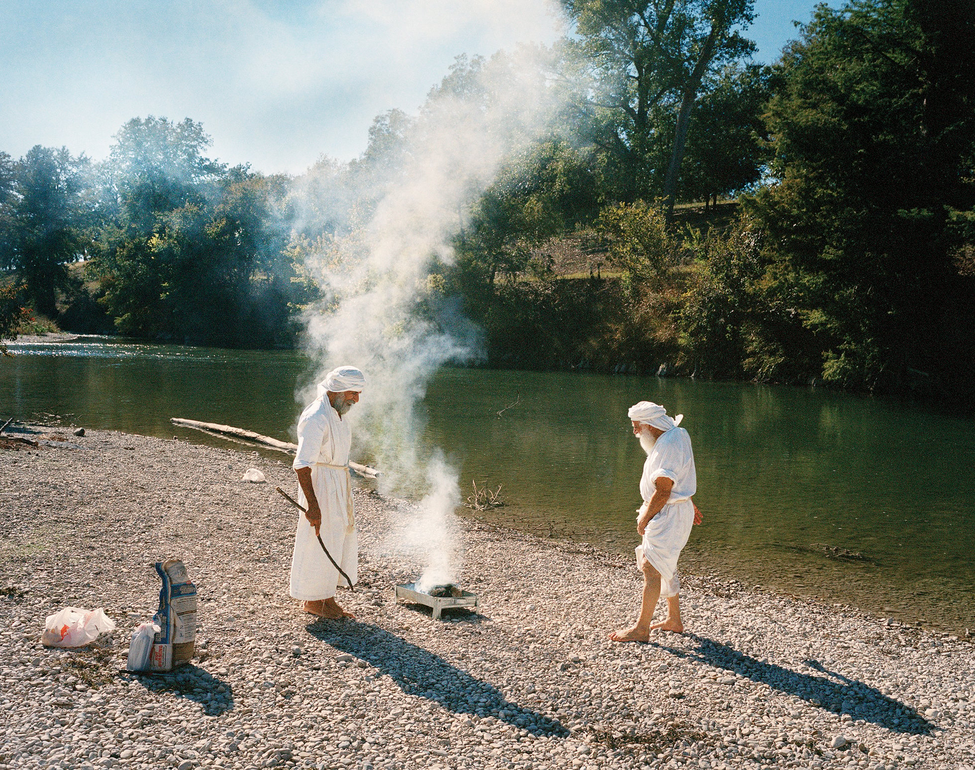 Shahram Ebadfardzadeh, left, and Hormoz Ebadeh Ahvazi prepare a fire during a day of remembrance at the Guadalupe River near San Antonio. They'll eat while praying for the souls of people who have died.