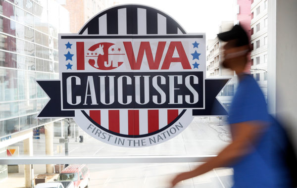 A pedestrian walks past a sign for the Iowa Caucuses.