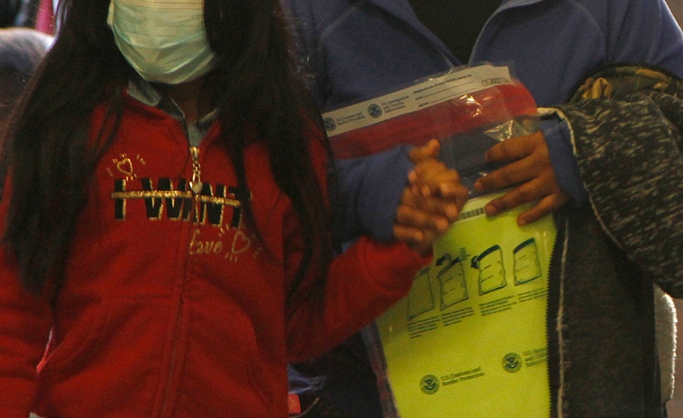 A woman carries a property bag issued by Customs and Border Protection while holding the hand of a girl wearing a mask as they arrive at a mandatory immigration court hearing on Monday, March 16, 2020, in El Paso, Texas. The migrants, who must wait in Ciudad Juarez, Mexico, wore masks following the first reported cases of COVID-19 in El Paso. The migrants are not suspected to be carrying the virus. (AP Photo/Cedar Attanasio)