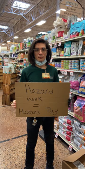 Joshua Cano holds protest sign reading "Hazard Work = Hazard Pay" in a Sprouts grocery store in McAllen.