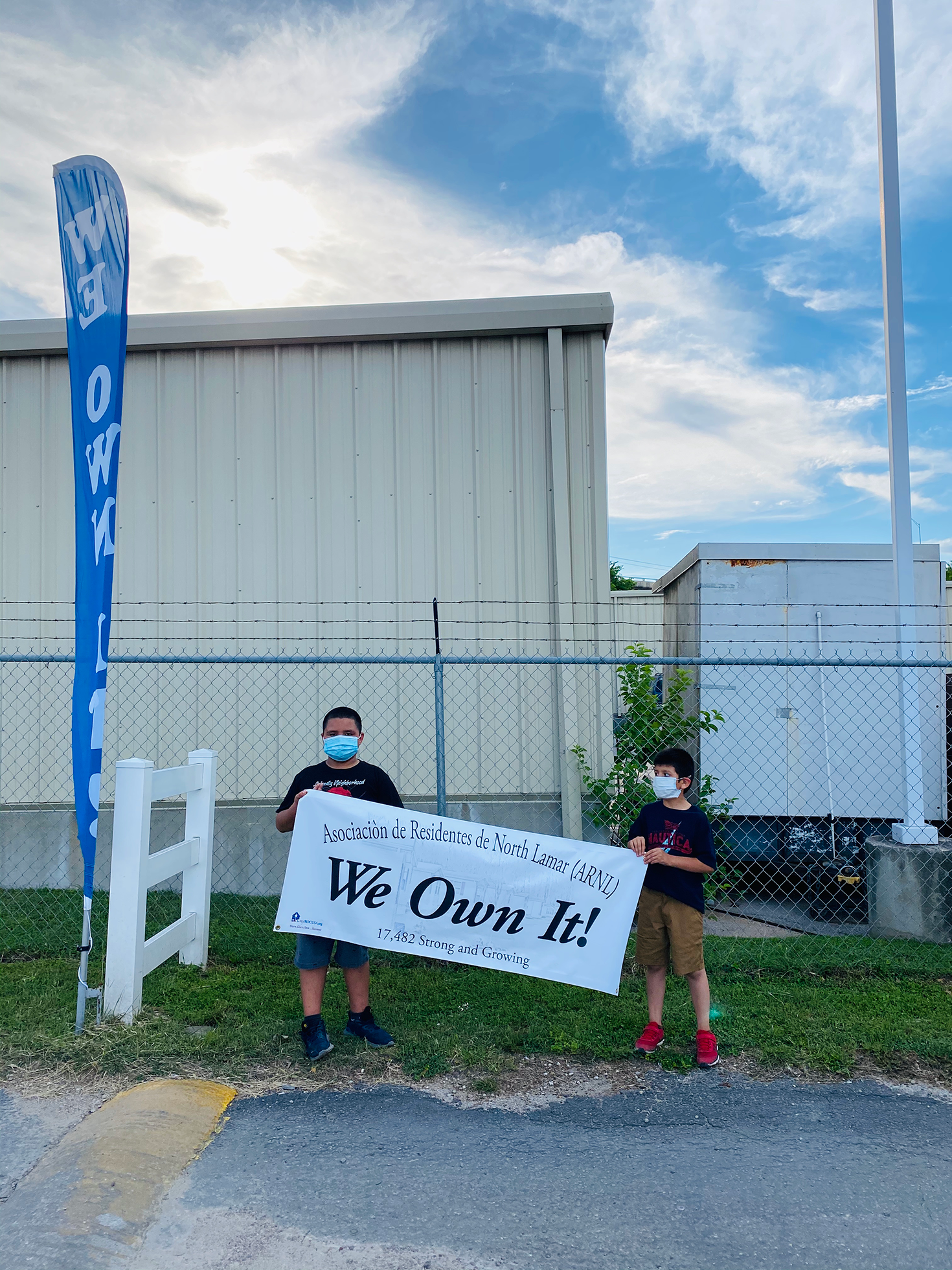 Two young kids hold a banner reading: Asociación de Residentes de North Lamar: We Own It!