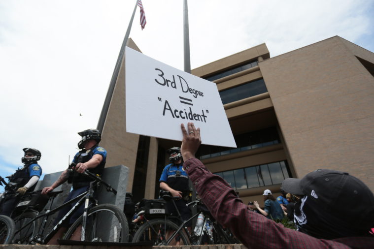 A protestor holds up a sign referring to police officer Derek Chauvin's third degree murder and manslaughter charges in relation to the killing of George Floyd.