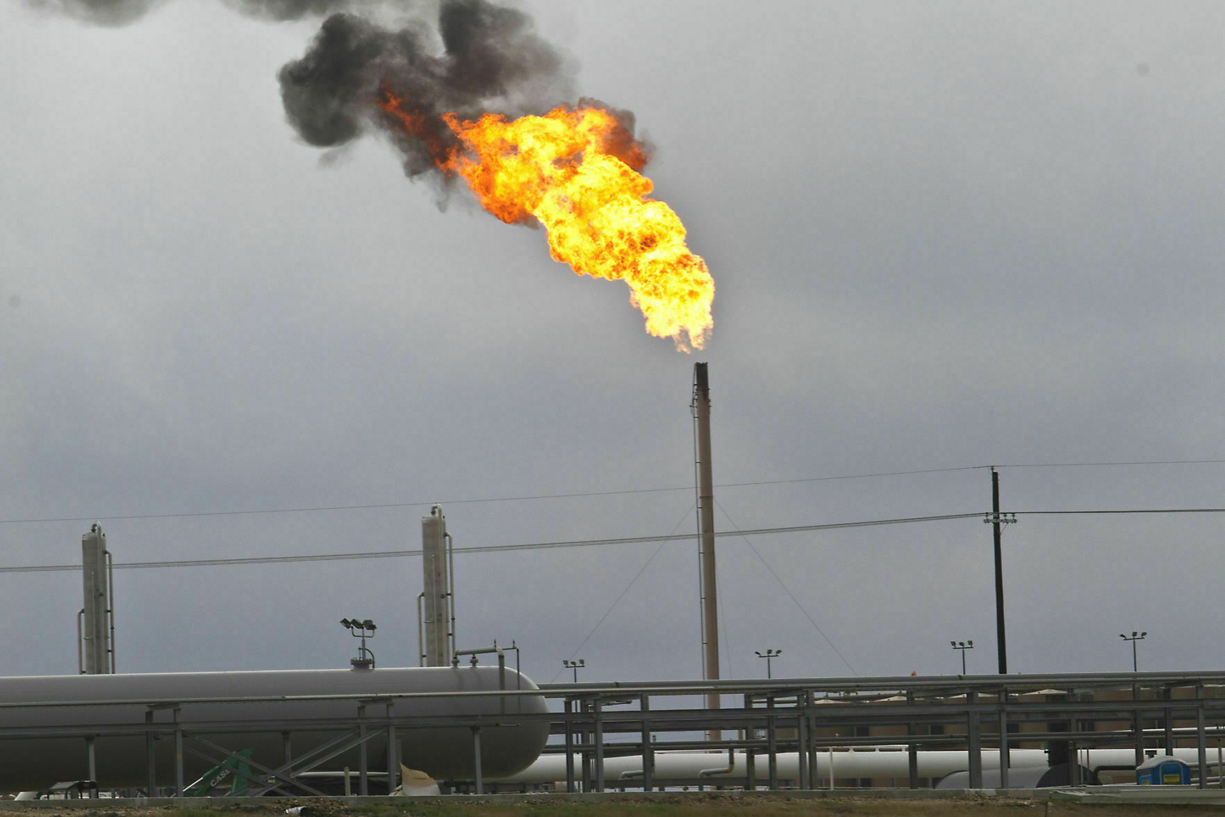 A burst of flame comes from a smokestack, reaching into a smoggy, cloudy sky.