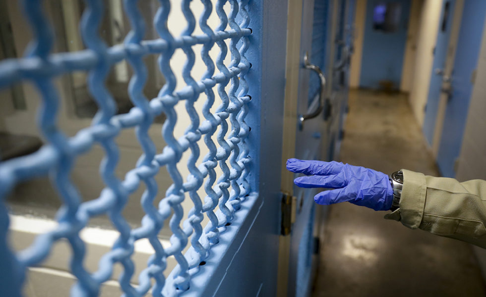 A gloved hand points to a holding cell at the hospital ward of a jail.