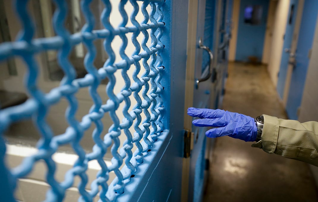 In this April 16, 2020, photo a gloved hand points to a holding cell at the hospital ward of the Twin Towers jail in Los Angeles. Across the country first responders who've fallen ill from COVID-19, recovered have begun the harrowing experience of returning to jobs that put them back on the front lines of America's fight against the novel coronavirus. (AP Photo/Chris Carlson)