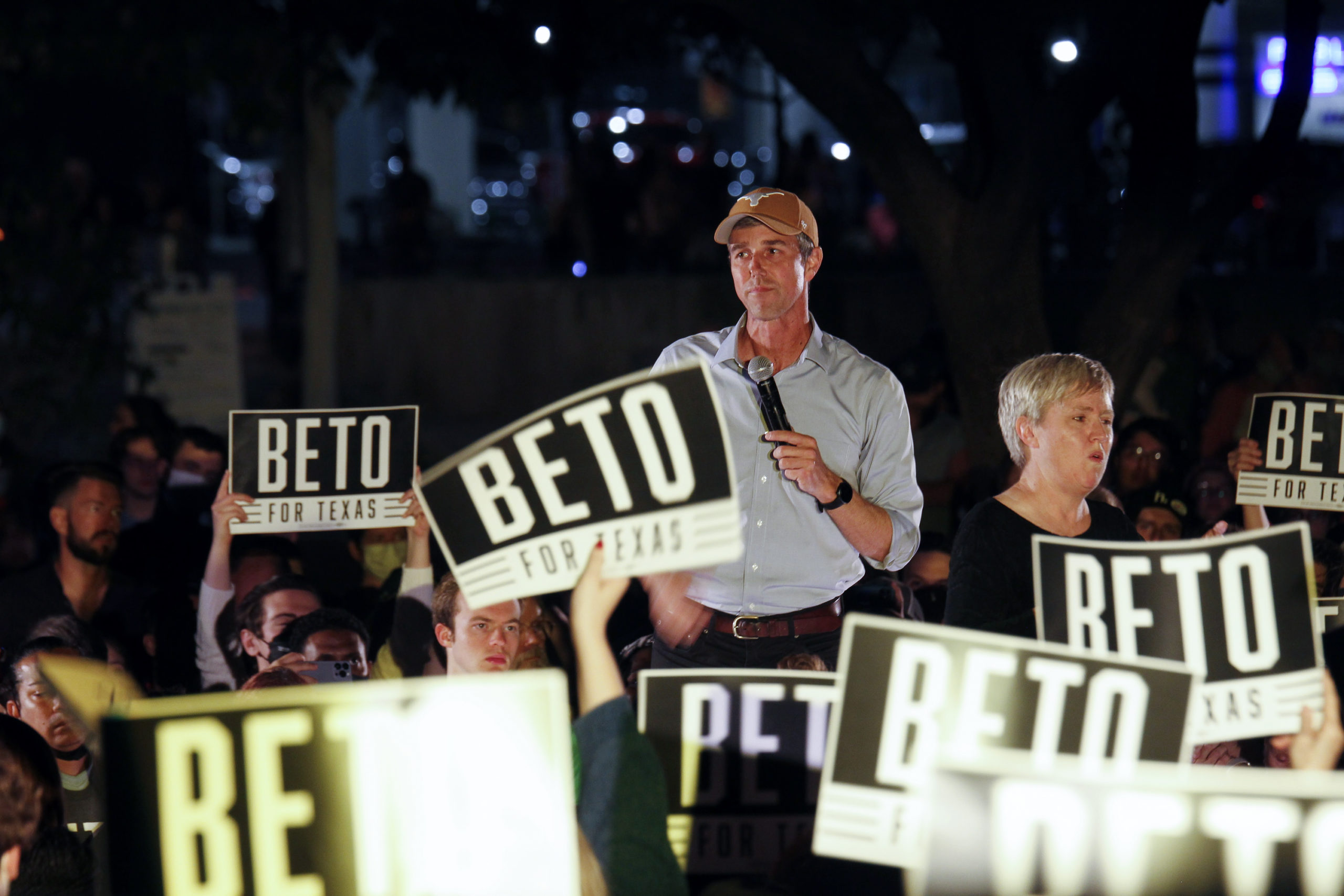 Beto O'Rourke stands at a rally, holding a microphone, with a distant expression. Around him, supporters hold BETO signs aloft. O'Rourke met defeat in the 2022 election despite spending 10s of millions.