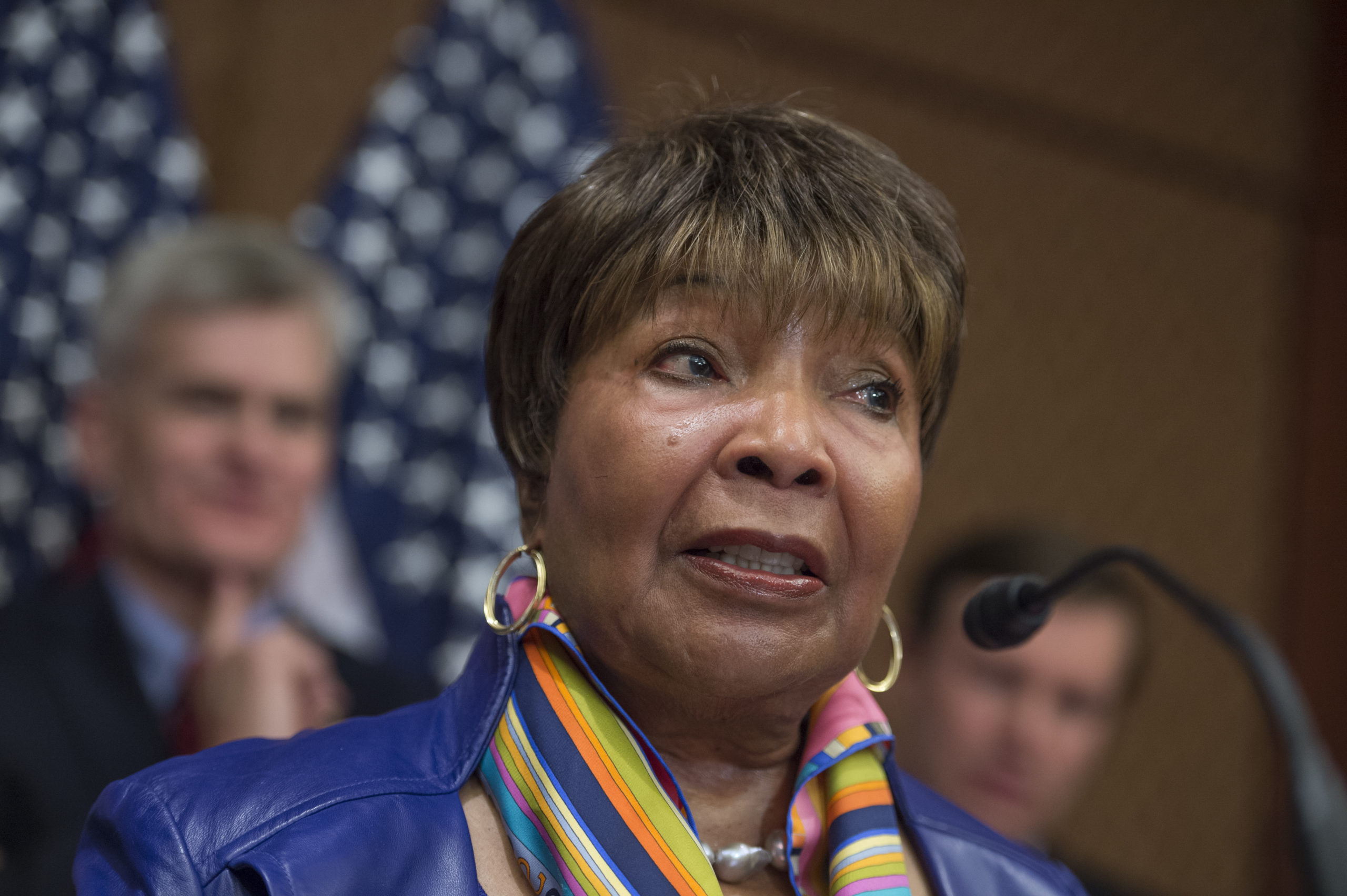 A color photo of Eddie Bernice Johnson, wearing a blue jacket, gold hoop earrings and a rainbow scarf.