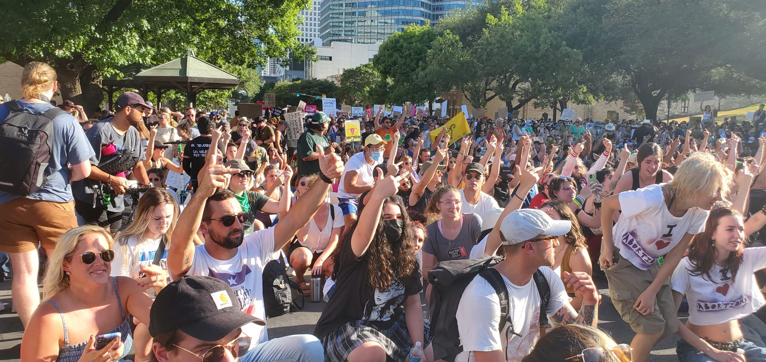 Sitting or squatting in the street outside the Texas Capitol, hundreds of marchers give the middle finger in protest of the overturning of Roe V. Wade