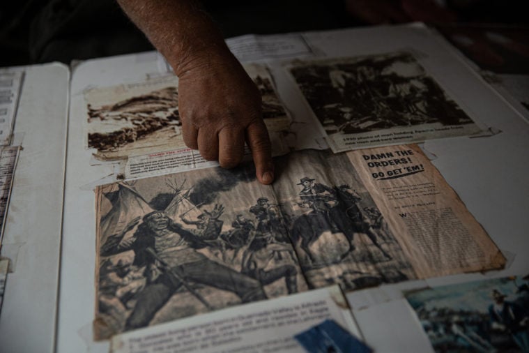 A hand points at a newspaper illustration depicting a violent raid.