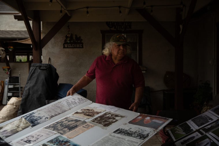 A Native American Man stands with a poster board covered with clipped articles and other printed matter.