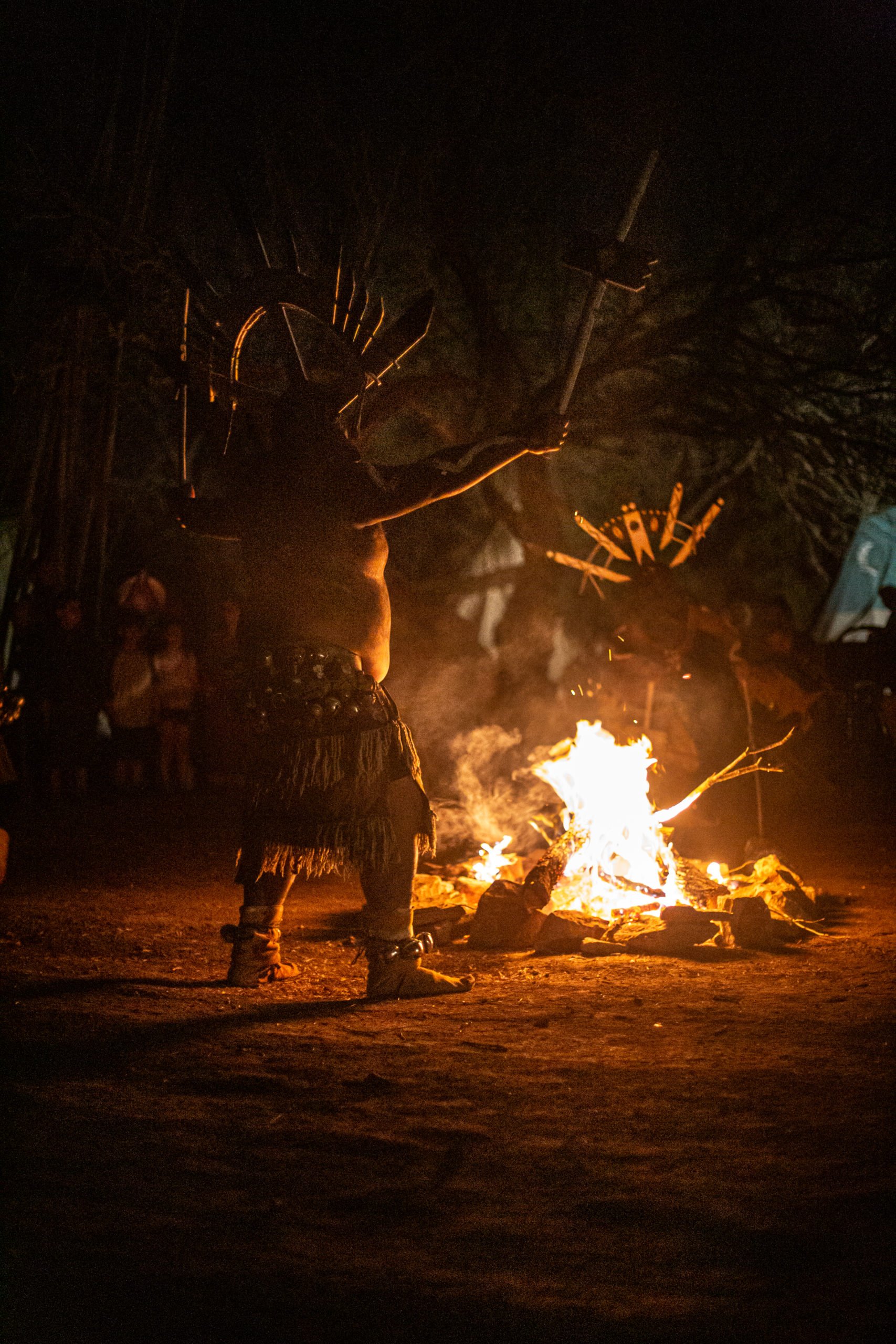 A man in Native American regalia dances in front of a fire.