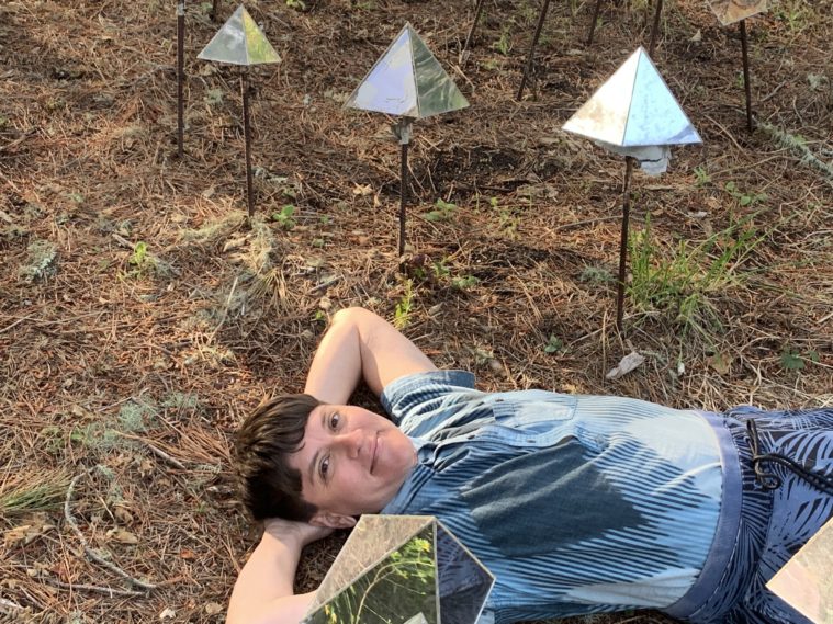 Amber Bemak, a white woman with short dark hair, lays in the grass with her hands behind her head.