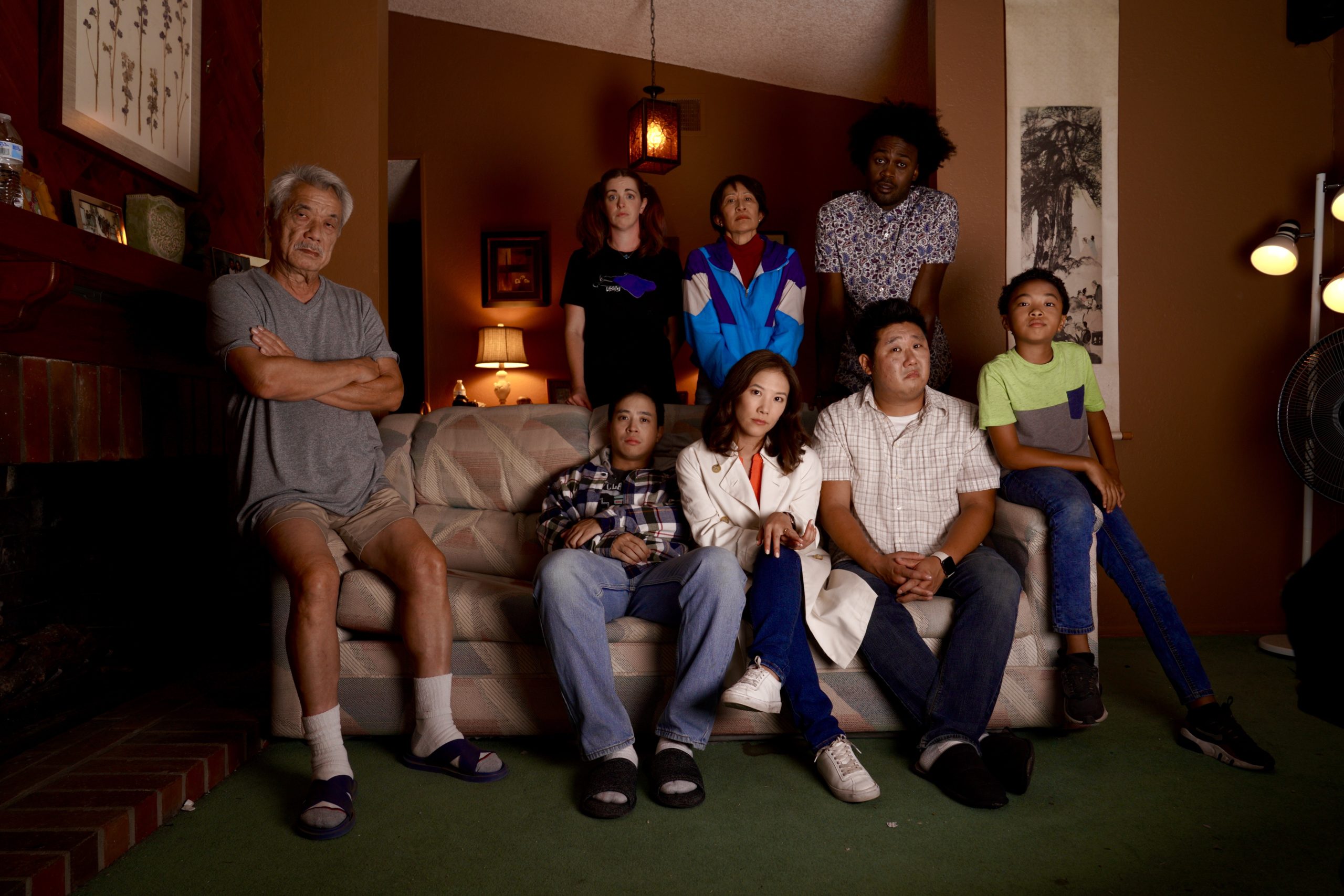 Dana Lee, an elderly Chinese man, sits with arms crossed on the edge of a couch, with the rest of the majority-Asian cast of "Dealing with Dad" posed around it.