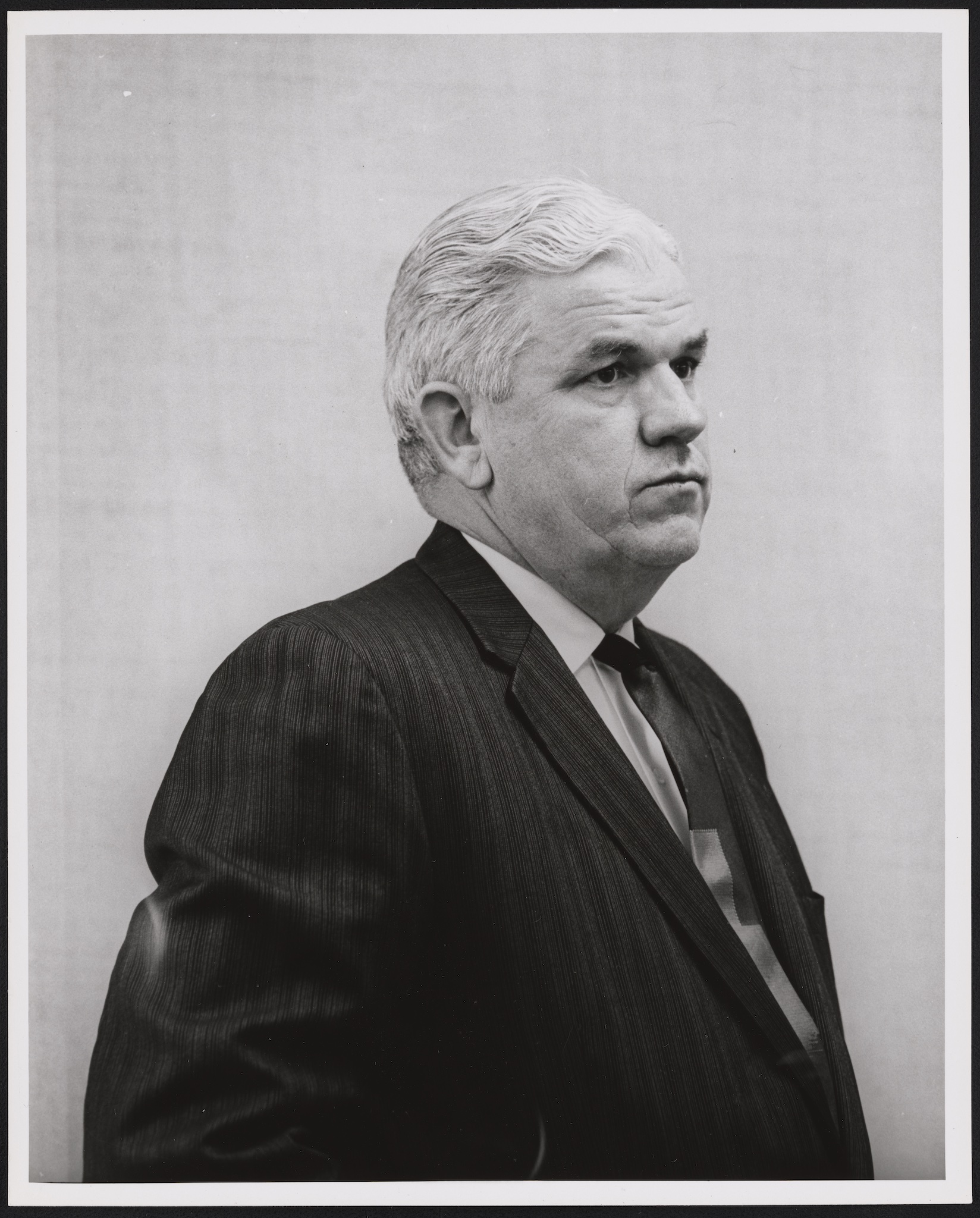 A black and white portrait of famous abortion prosecutor Henry Wade, a white man with gray hair and a round face, looking to the right with a serious expression. He's wearing a traditional suit and tie.