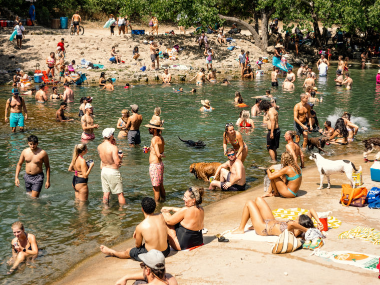 Dozens of people, along with some pet dogs, swim and lounge on the concrete side of the natural Barton Springs waterway.