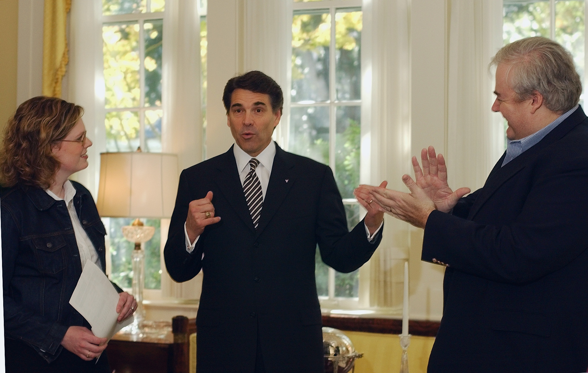 Rick Perry, in a suit, wears a surprised and excited expression as two political operatives cheer him on.
