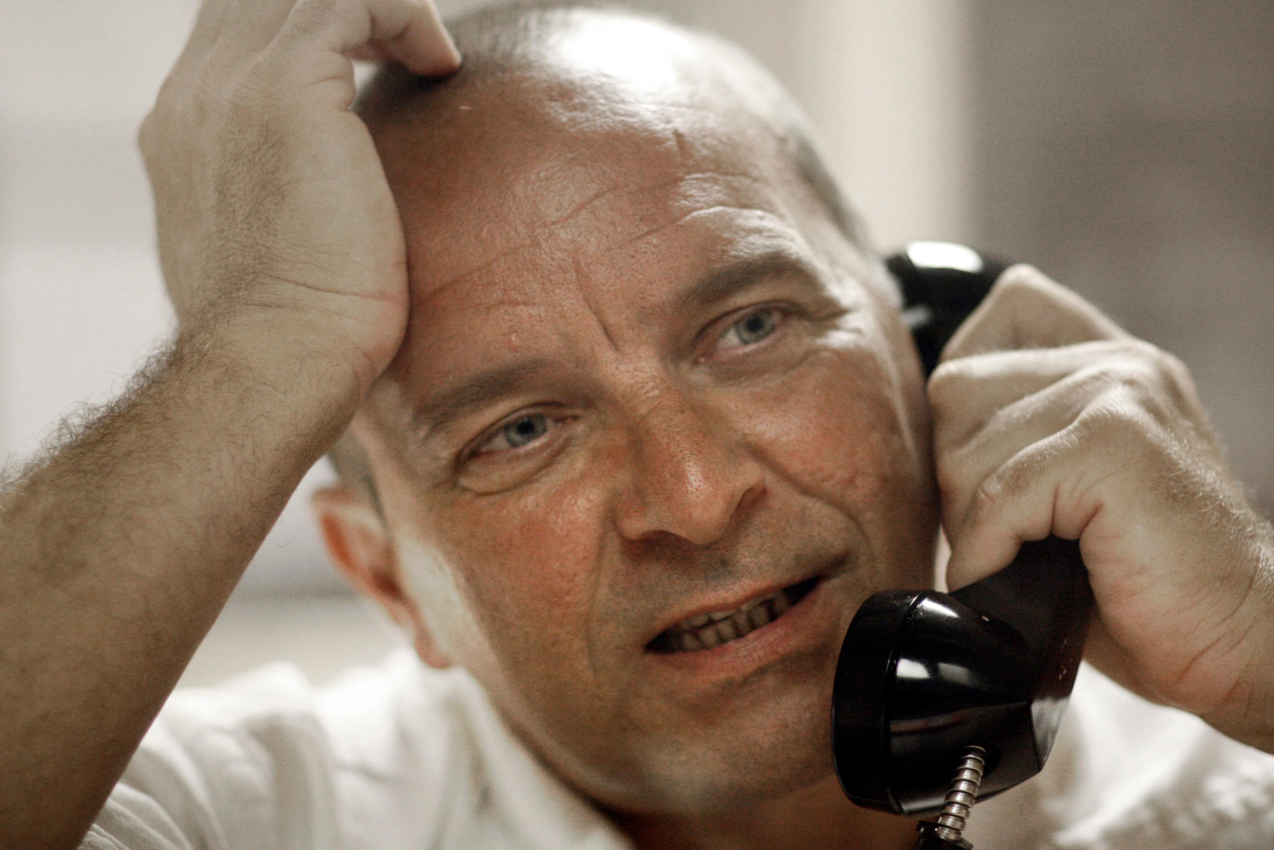 Elmer Wayne Henley, a bald white man, is seen resting his head on his hand as he speaks into a telephone handset during a prison interview.