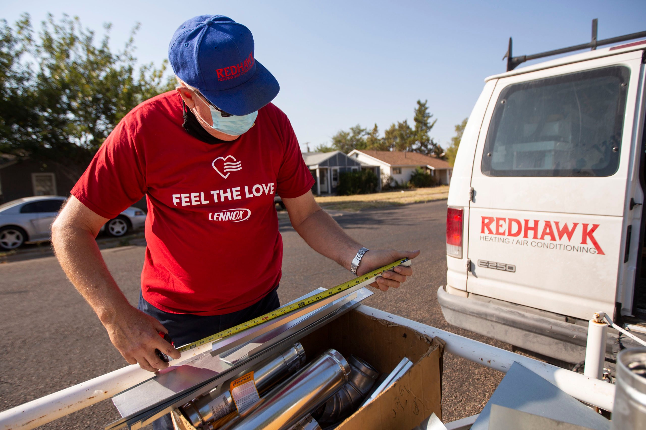 An HVAC technician in a hat and mask measures ductwork before bringing it inside a home from his van, in Odessa, Texas.