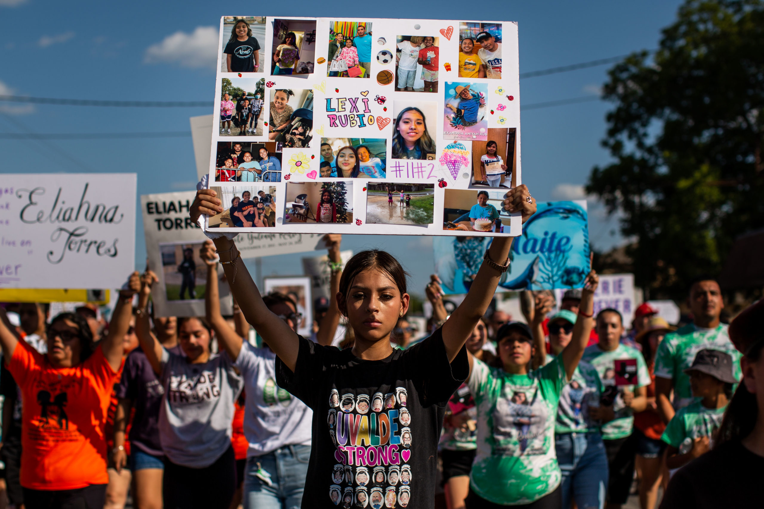 A young woman holds a sign at the head of a protest march in Uvalde July 10.