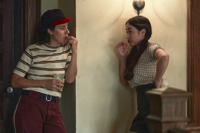 Roberta Colindrez leans against a wall as she speaks, in character, to another Latinx actress standing just around a corner from her.