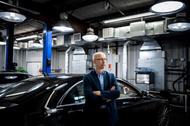 Peter Stout, the President and CEO of the Houston Forensic Science Center (HFSC), poses for a portrait while touring an annex where vehicles that were recovered from crime scenes are sent for evidence processing. He is wearing glasses, a blue suit jacket and blue botton-down shirt.