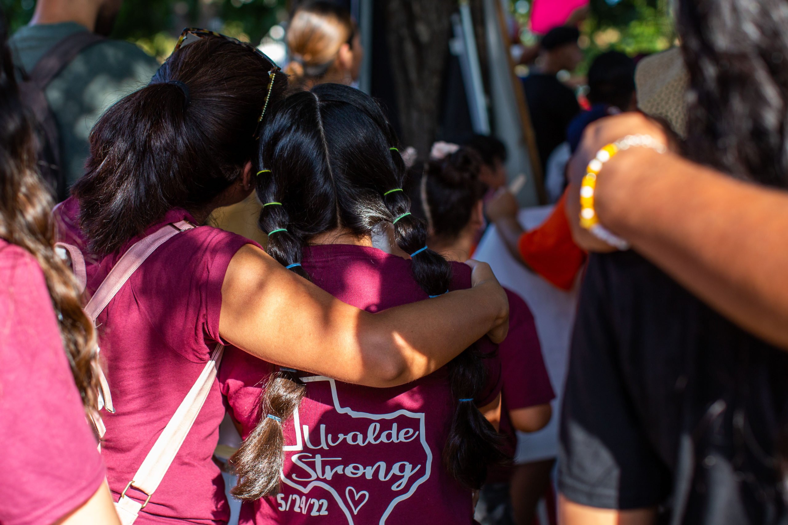Two women embrace at the Unheard Voices March & Rally for the 21 victims of the Robb Elementary mass shooting in Uvalde, Texas, on July 11, 2022. They are wearing red "Uvalde Strong" t-shirts.