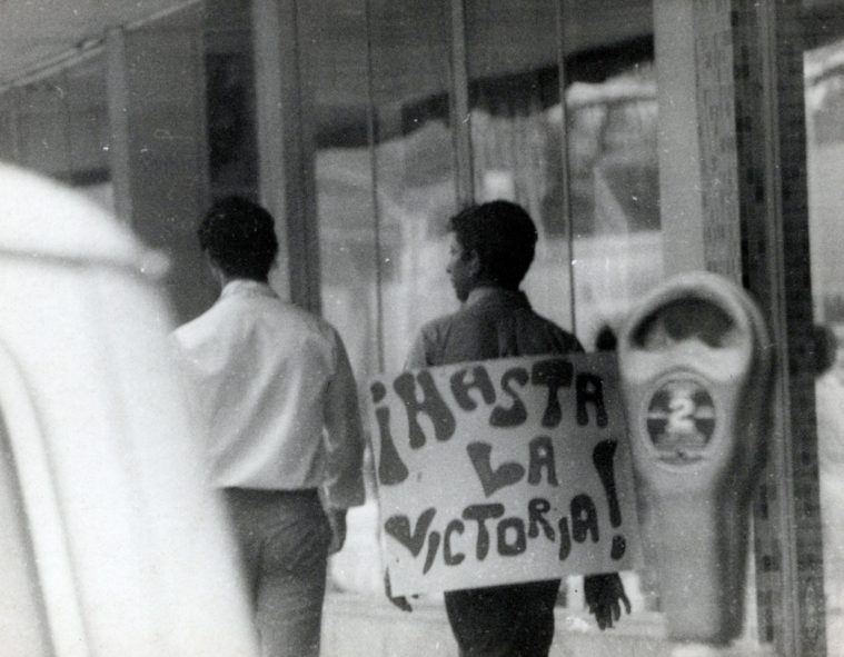 A protester walks away from the camera with a sign reading "Hasta La Victoria" in Uvalde in 1970