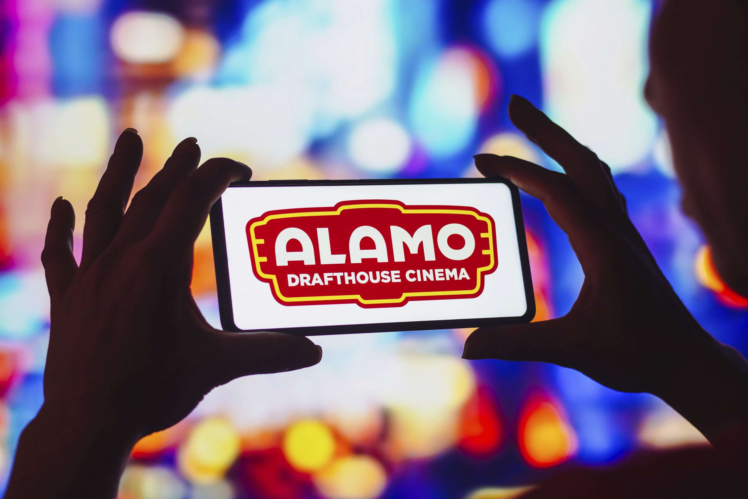 A silhoutte of a face and hands holding a smartphone, which has the Almao Drafthouse Cinema logo on it.