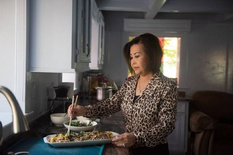 Hue Hoe, a Vietnamese woman in a leopard print jacket, arranges a meal on a platter using chopsticks in a well-appointed kitchen.