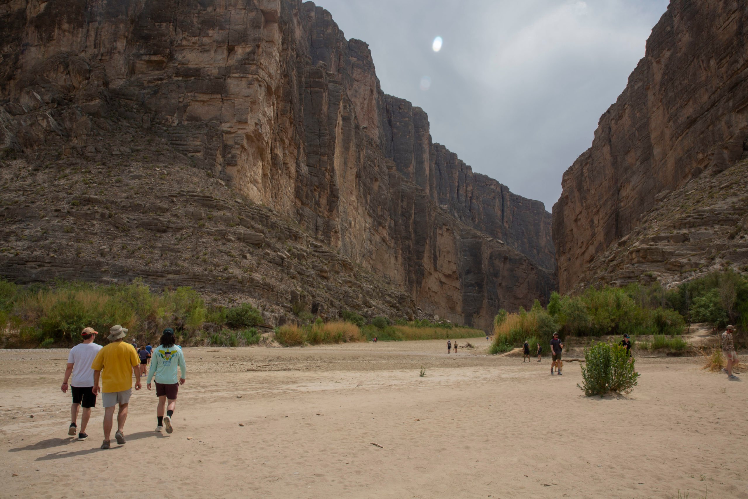 A trio of tourists gaze upon the empty river bed of the Rio Grande, which normally runs through the tall canyon walls seen here.