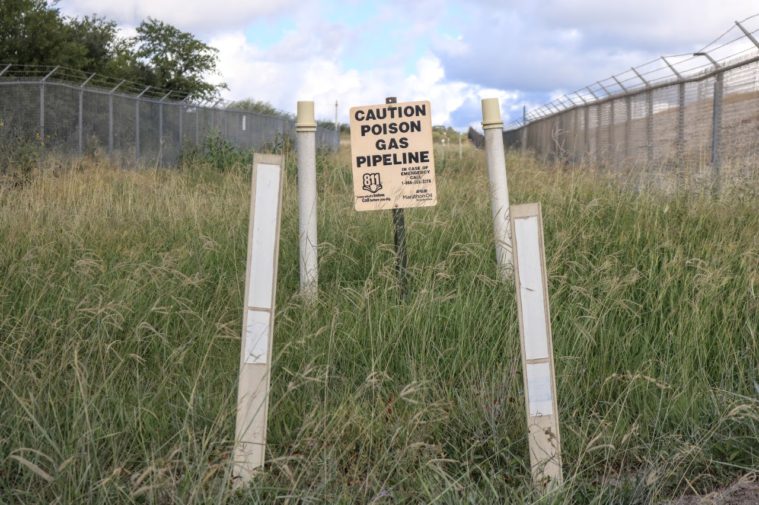 A sign warns of a "Poison Gas Pipeline" set amid fencing and thick grass.